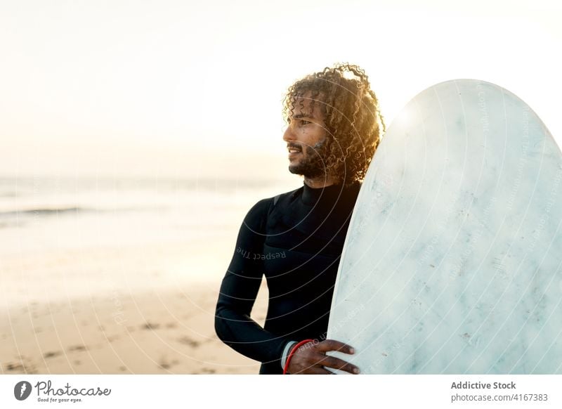 Cheerful surfer holding skimboard man cheerful sunset seashore freedom tropical water sports male resort ethnic ocean beach summer swimsuit guy surfboard