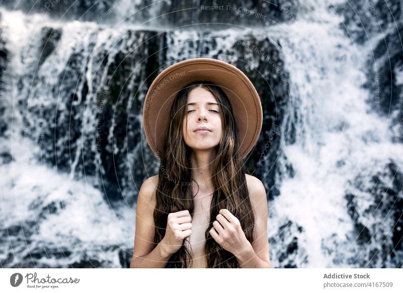 Calm naked woman near waterfall in summer fresh air enjoy nature nude cover breast female tranquil eyes closed sensual relax long hair body spectacular natural