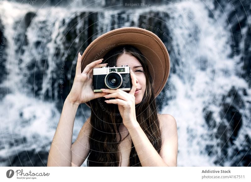 Stylish woman taking photo on vintage camera photo camera traveler take photo retro old fashioned water nature waterfall female vacation hat trendy amazing