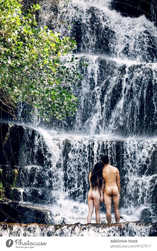 Unrecognizable naked couple near waterfall nude nature enjoy scenery calm close relationship summer together body rock romantic love sensual boyfriend