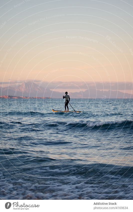 Man in wetsuit on paddleboard in sea man surfer row sup training male summer sport water sunset nature enjoy professional sportsman fit confident guy alone