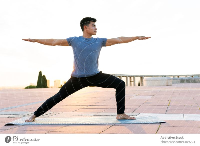 Ethnic man in sportswear doing yoga at sunset warrior pose practice asana flexible focus tranquil male ethnic asian virabhadrasana urban park mat healthy