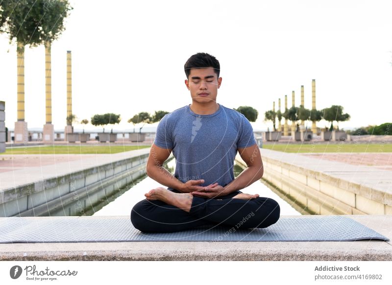 Tranquil man mediating in Lotus pose in park lotus pose meditate yoga harmony asana padmasana flexible legs crossed practice male ethnic asian mat relax calm