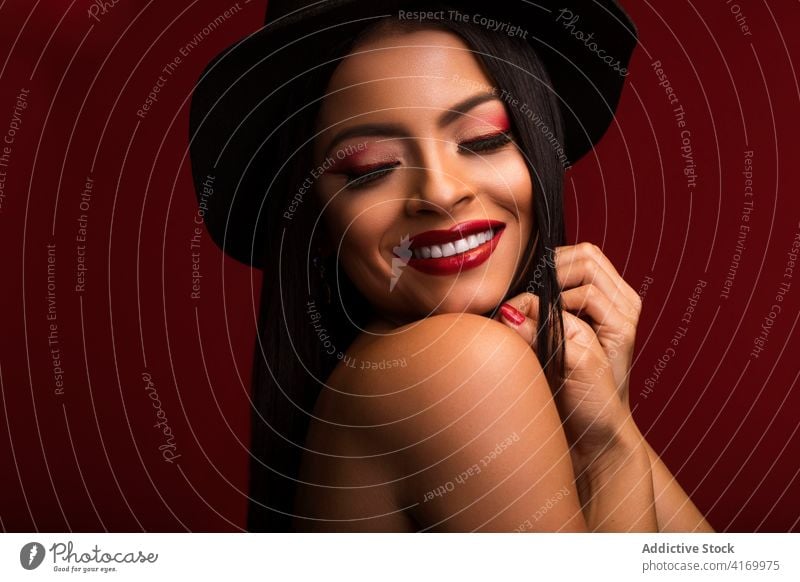 Smiling woman with red lips in studio makeup visage charming appearance hat touch head model cheerful female smile optimist positive content vivid vibrant