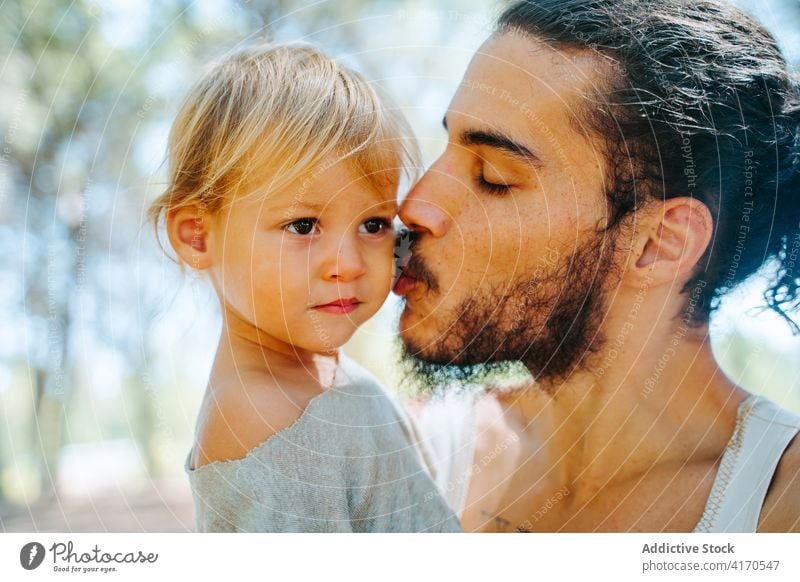 Happy father kissing cute kid in forest child cheek love tender together weekend ethnic multiracial diverse parenthood fatherhood adorable hipster enjoy