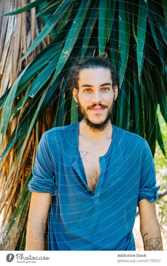 Ethnic man standing in nature park male ethnic long hair bun hairstyle tropical relax calm healthy tranquil peaceful summer serene tree exotic garden freedom