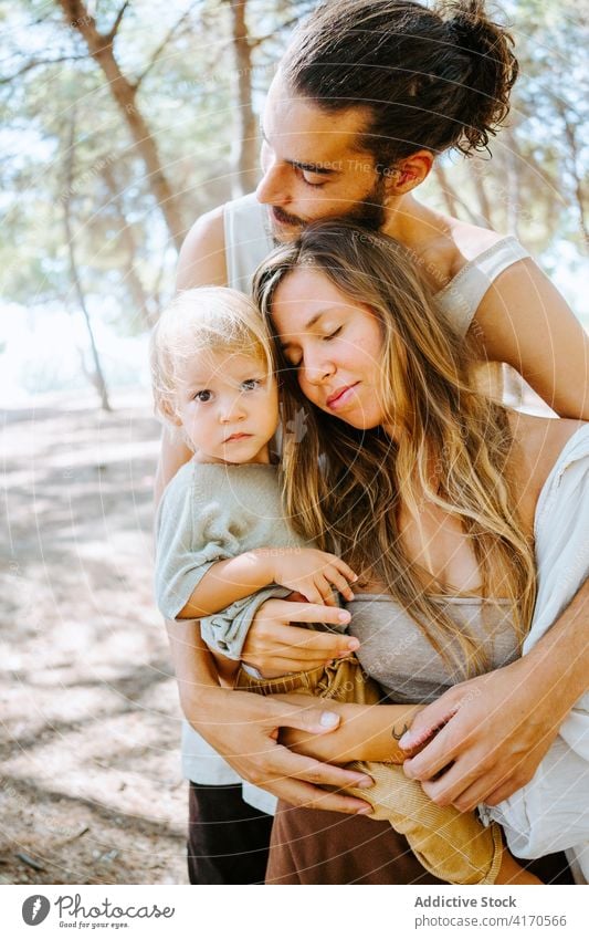 Happy multiethnic family hugging with eyes closed in forest woods weekend together toddler kid love unity multiracial diverse nature embrace relationship