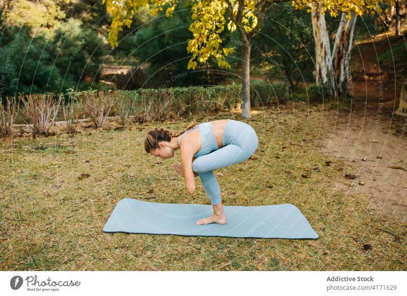 Flexible woman doing one legged balancing yoga pose in park one legged chair eka pada utkatasana practice balance stand bend forward female wellness lifestyle