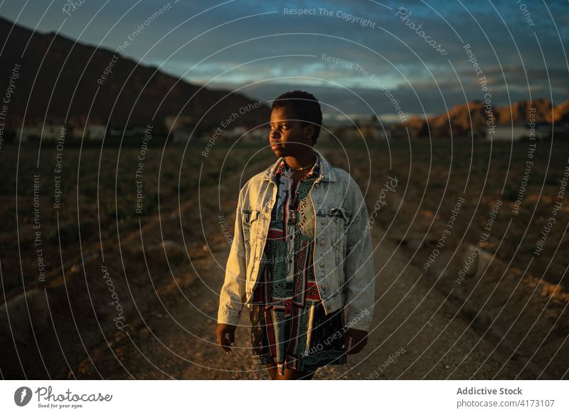 Female traveler walking along countryside road in mountainous valley village sunbeam lit sunlight sunset highland tourist nature black african american trip