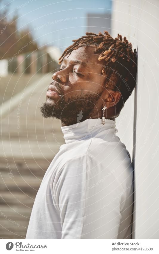 Stylish black man on city street carefree enjoy sunlight harmony relax urban dreadlocks individuality male ethnic african american building eyes closed tranquil