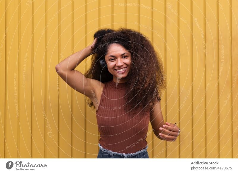 Charming ethnic woman with headphones on street curly hair afro hairstyle charming smile natural beauty female listen black african american city trendy rest