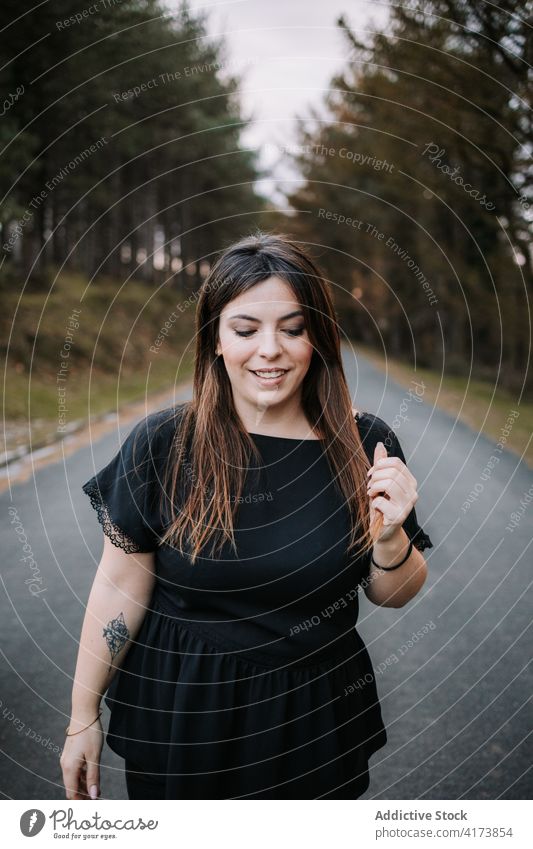 Smiling woman on road in forest smile roadway empty charming cheerful coniferous woods female content tree countryside joy style trendy harmony plump chubby