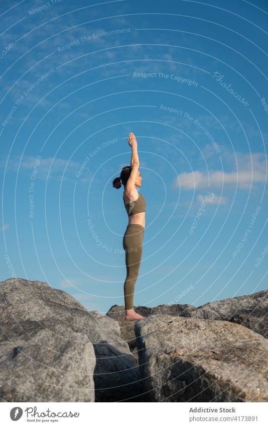 Focused woman practicing yoga on rock relax stone blue sky nature mindfulness zen female asana practice wellness harmony wellbeing calm lifestyle vitality