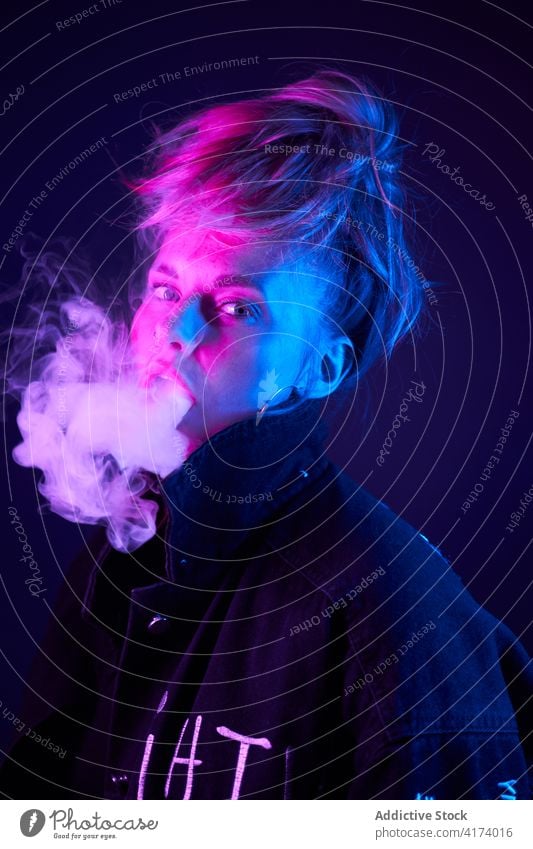 Expressive woman smoking in dark studio vape smoke e cigarette neon light steam cool female style nicotine smoker habit confident young bad unhealthy addict