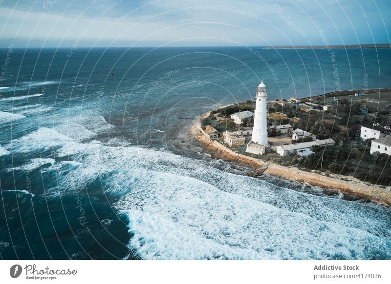 Lighthouse on coast near waving sea lighthouse wave tower beacon ocean shore navigate location water seaside seashore travel coastline foam marine shoreline