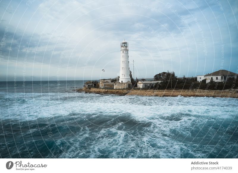 Lighthouse on coast near waving sea lighthouse wave tower beacon ocean shore navigate location water seaside seashore travel coastline foam marine shoreline