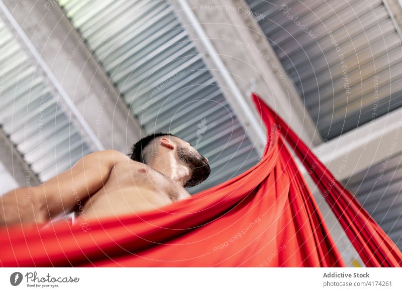 Shirtless male dancer with red cloth man fabric grasp rehearsal studio silk shirtless gymnast practice adult ribbon ceiling choreography acrobatic perform art