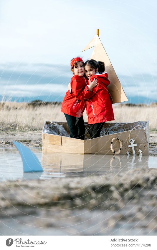 Playful girls standing in carton boat and having fun cardboard frighten shark scare imagination child play together inspiration game creative handmade pretend