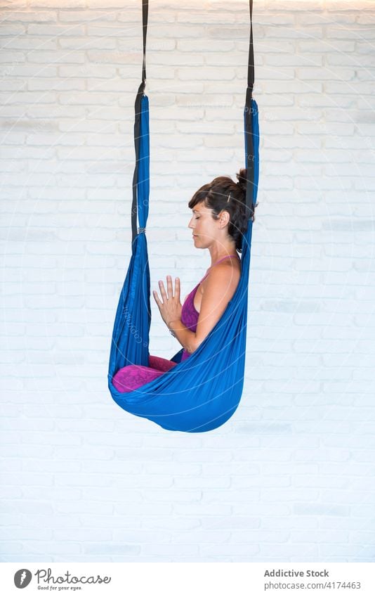 Woman meditating in hammock in studio woman meditate aerial yoga lotus pose zen hands clasped eyes closed female adult pilates harmony wellness spirit balance