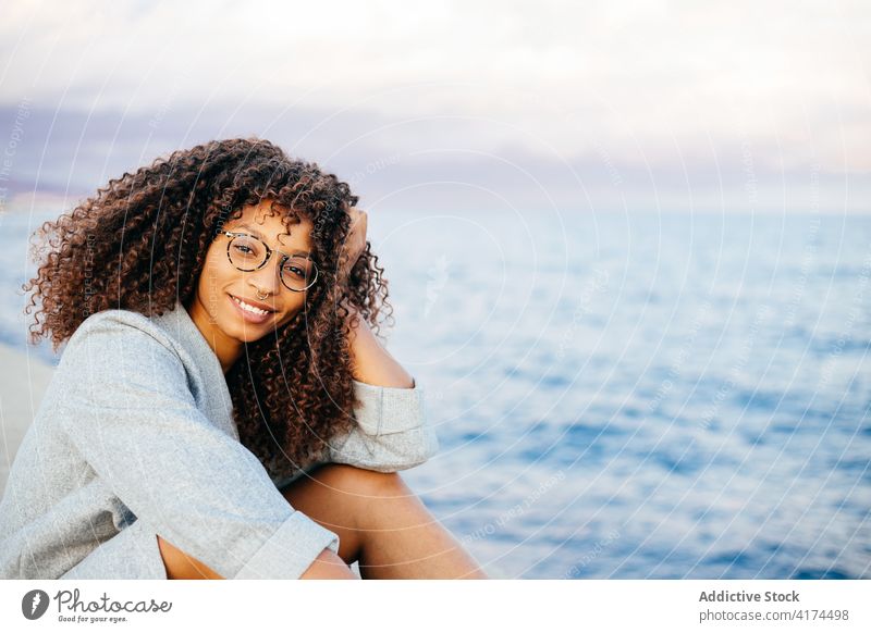 Cheerful black female sitting on embankment woman sea smile style weekend happy outfit rest young quay cheerful ethnic african american water delight relax