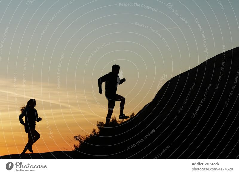 Athletes running in mountains at sunset silhouette runner training rocky terrain sundown summer sportswoman sportsman highland dusk evening twilight harmony