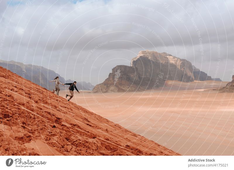 Carefree traveling couple running down hill in desert carefree sand freedom enjoy sandstone valley wadi rum jordan nature tourism adventure journey landscape