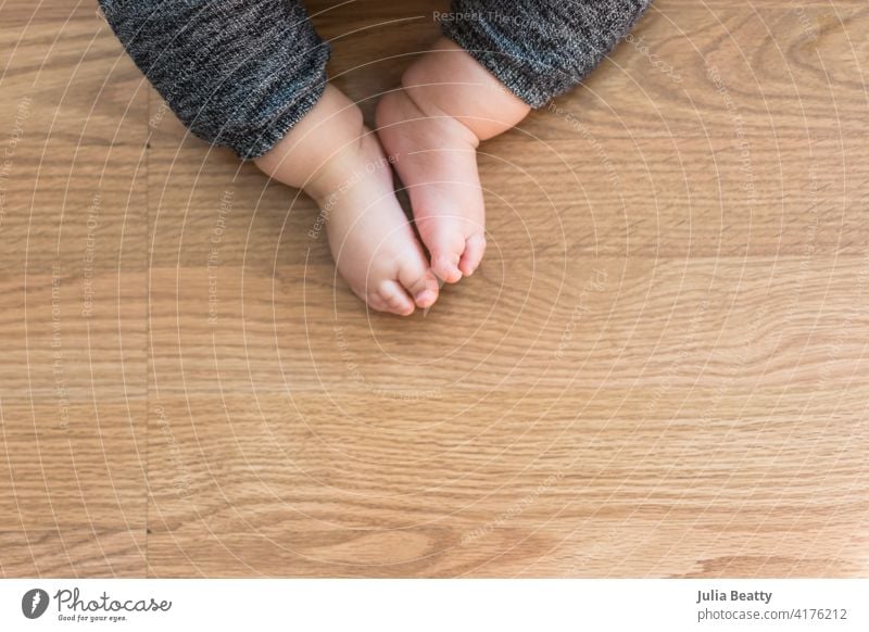 Toddler seated on laminate floor; feet touch each other as legs splay out in open seated pose similar to butterfly pose in yoga toddler independent milestone