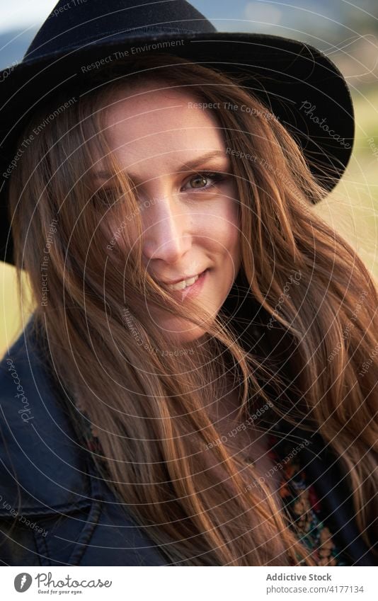 Charming woman in hat and leather jacket in countryside style sunset trendy outfit charming field female black apparel braid hairstyle long hair appearance