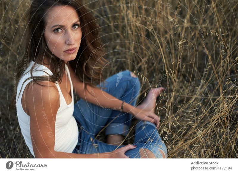 Dreamy woman sitting on grassy meadow daydream field nature countryside harmony relax contemplate carefree content thoughtful pensive rural solitude tranquil