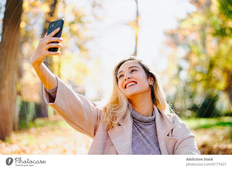 Woman taking selfie on smartphone in park woman autumn style relax entertain self portrait take photo female sunny sit weekend social media gadget device season