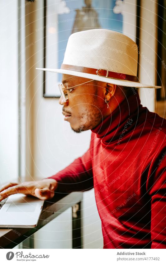 Stylish black businessman in cafe on computer entrepreneur style elegant remote male ethnic hat african american trendy break work freelance netbook laptop