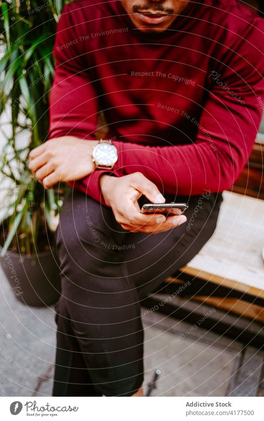 Anonymous black man browsing smartphone near cafe in city surfing social media street style trendy male ethnic african american internet mobile phone online