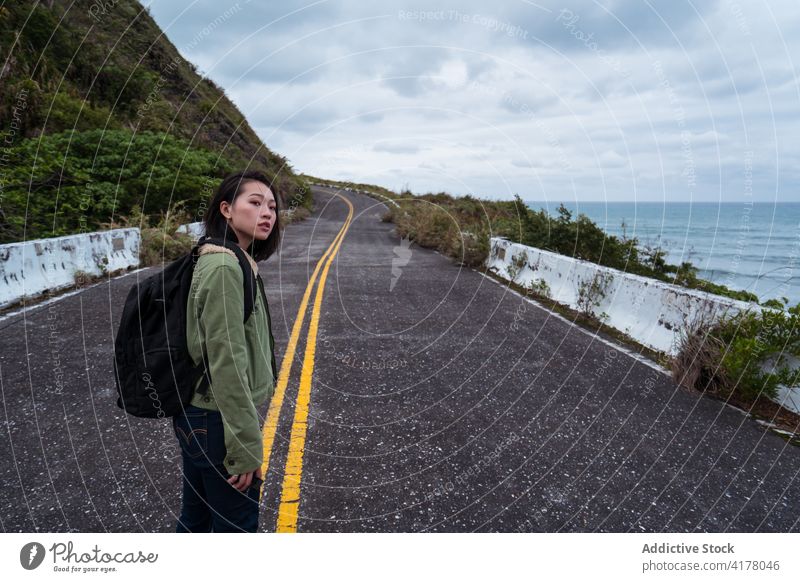 Woman with backpack walking on road on seashore traveler coast rocky woman ocean stormy adventure female active hiker backpacker nature direction route roadway