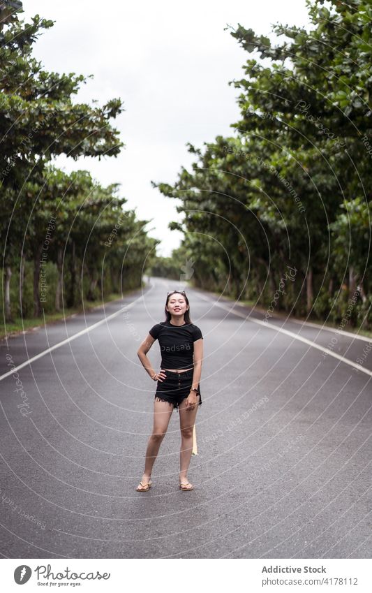 Young woman standing on asphalt road in forest park traveler positive way path nature explore young asian female ethnic kenting taiwan active tree happy smile