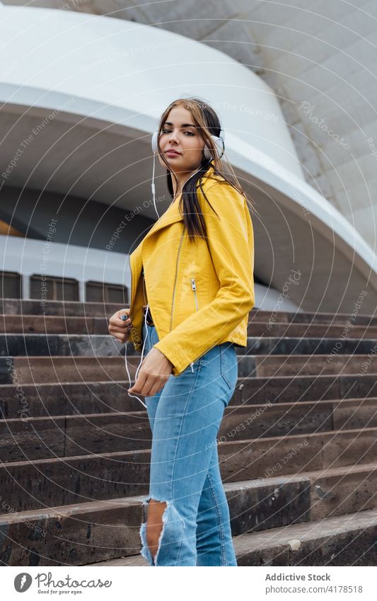 Hipster woman with headphones standing on street hipster trendy listen urban style stair music young female jeans denim gadget device lifestyle enjoy optimist