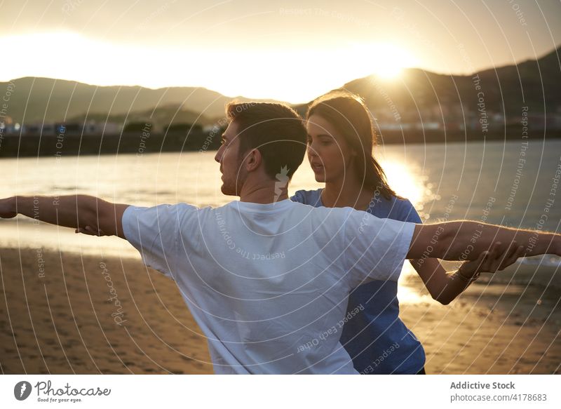 Man doing yoga in Warrior pose with help of instructor practice man support healthy warrior pose sea beach sunset female trainer wellbeing mindfulness together