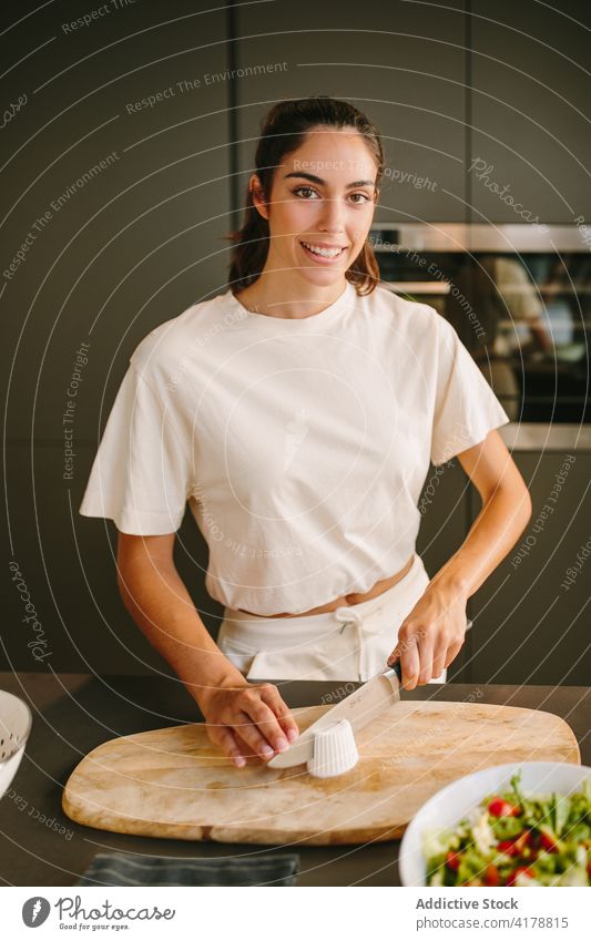 Smiling woman cutting cheese for salad in kitchen feta prepare cook vegetable delicious home female homemade knife healthy cutting board gourmet yummy culinary