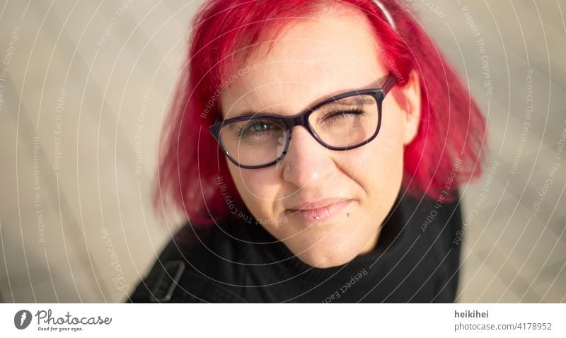 A redheaded woman with glasses and piercings looks into the camera winking Woman Eyeglasses Red-haired portrait Lip piercing conspicuous appearance Emanation