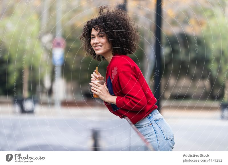 Smiling black woman with cup of takeaway juice in street city enjoy weekend to go plastic relax female ethnic african american fresh afro hairstyle curly hair