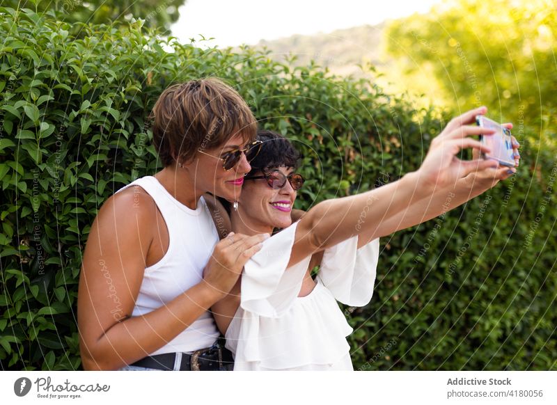 Smiling women taking selfie in park friend together memory summer enjoy self portrait smartphone adult female green mobile style cheerful weekend trendy