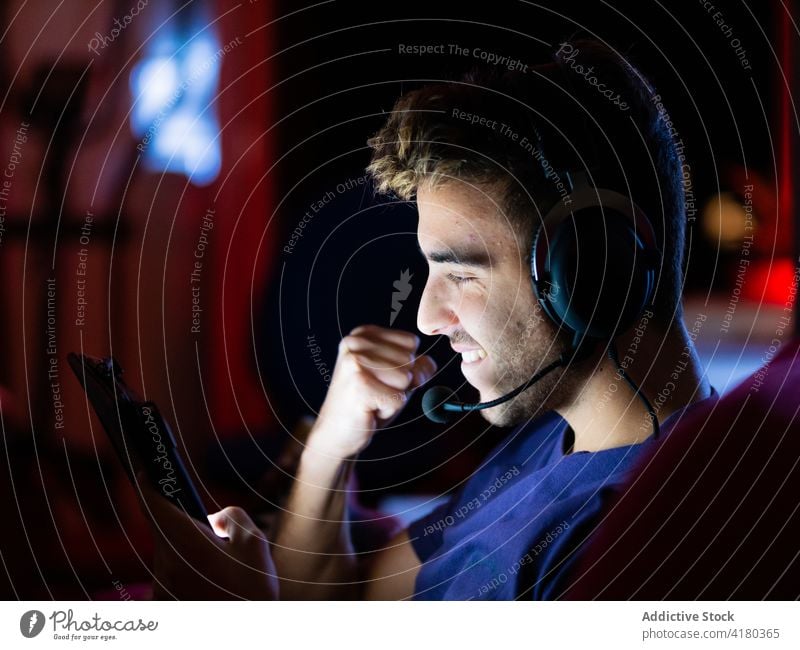 Man in headphones using tablet and raising fist in excitement man fist up excited victory triumph joy celebrate win device gadget achieve browsing luck winner