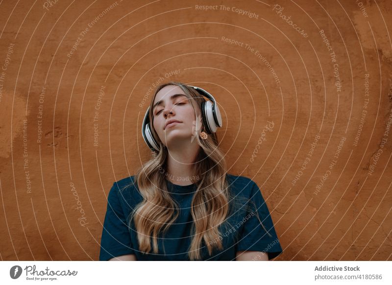 Dreamy woman listening to music in headphones in town song eyes closed thoughtful enjoy dreamy wireless using gadget street device headset modern style melody