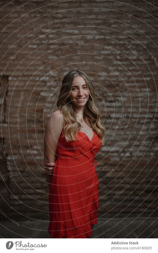 Glad traveler in sundress against brick wall on street tourist smile hand behind back enjoy spare time weekend town woman red cloth trip vacation romantic