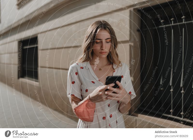 Young woman with smartphone on city street candid focus friendly spare time weekend blonde charming pavement urban mask covid 19 unemotional lifestyle gadget