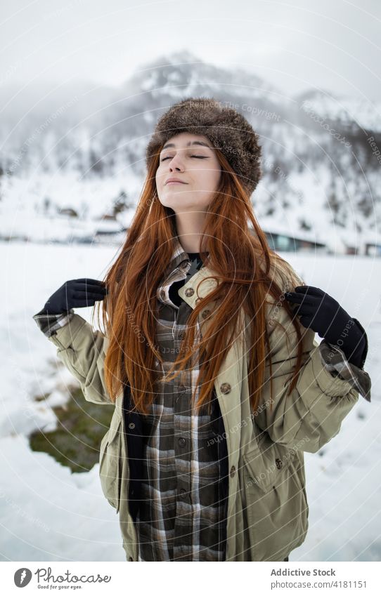 Dreamy traveler in outerwear against snowy mountain eyes closed breathe enjoy harmony idyllic winter woman ornament glove wellness trip journey vacation