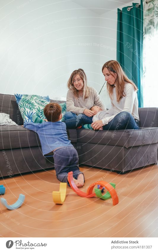 Happy lesbian couple on sofa looking at playing son family cheerful mother alternative lgbtq joy at home homosexual adorable relationship love happy parent