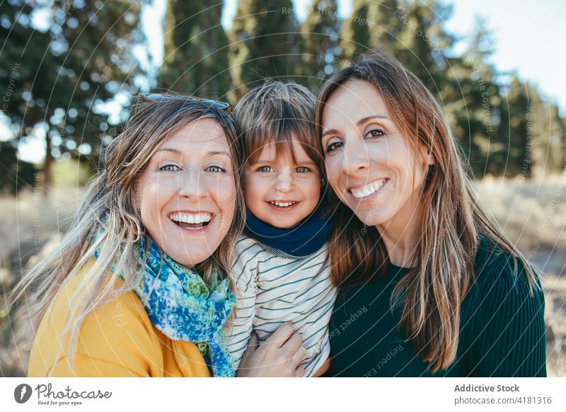 Smiling lesbian couple hugging with son in nature toothy smile embrace family joy lgbt spend time cheerful homosexual lgbtq adorable relationship love happy