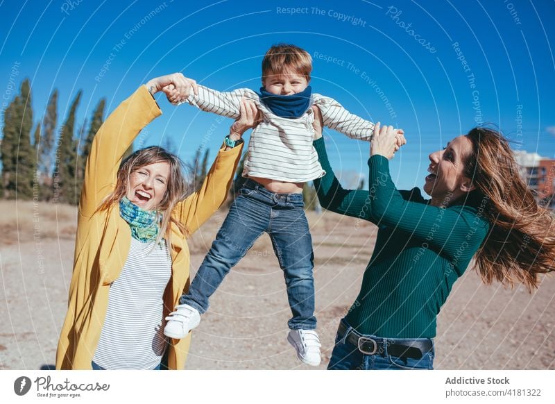 Cheerful lesbian couple raising cute son on hands on beach family joy lgbt cheerful arms raised nature homosexual lgbtq adorable relationship love happy parent