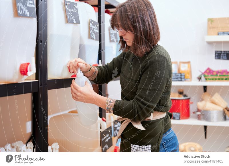 Young woman pouring eco detergent into bottle chemical agent sustainable store faucet female seller work zero waste ecology small business service retail shop