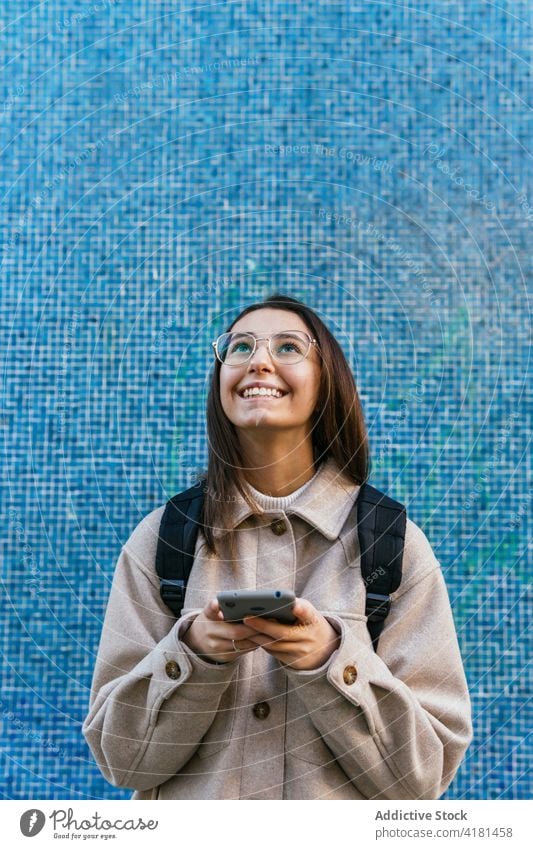 Cheerful woman browsing smartphone on street student using toothy smile backpack commute urban happy surfing beautiful chat cellphone free time cheerful gadget